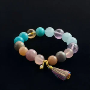 Natural crystal beaded bracelet featuring teal Amazonite, pale blue Aquamarine, and Gray Flash Spirit Moonstone with a tassel charm on a black background. Healing jewelry for Throat Chakra and anxiety relief.