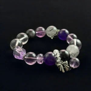 A genuine crystal bracelet featuring round purple amethyst beads, clear quartz with black rutile needles, and solid black obsidian beads, accented with silver flower and butterfly charms on a dark background.