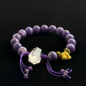 Charoite gemstone bracelet with a central clear quartz crystal point, gold Feng Shui charms, and adjustable purple cord on a black background