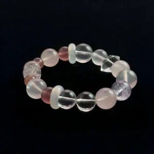 A top-down view of a multi-gemstone crystal bracelet on a black background. It features bead of reddish strawberry quartz, pale pink quartz, translucent white agate, a single purple amethyst bead, clear quartz spheres, and a central carved clear quartz Pixiu figure.