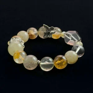 This describes the image for visually impaired screen readers and tells Google exactly what is in the picture. A detailed view of a beaded crystal bracelet on a black background, featuring golden rutilated quartz spheres, translucent yellow phantom quartz beads, a faceted reddish quartz bead, clear quartz, and a silver metal moth charm.