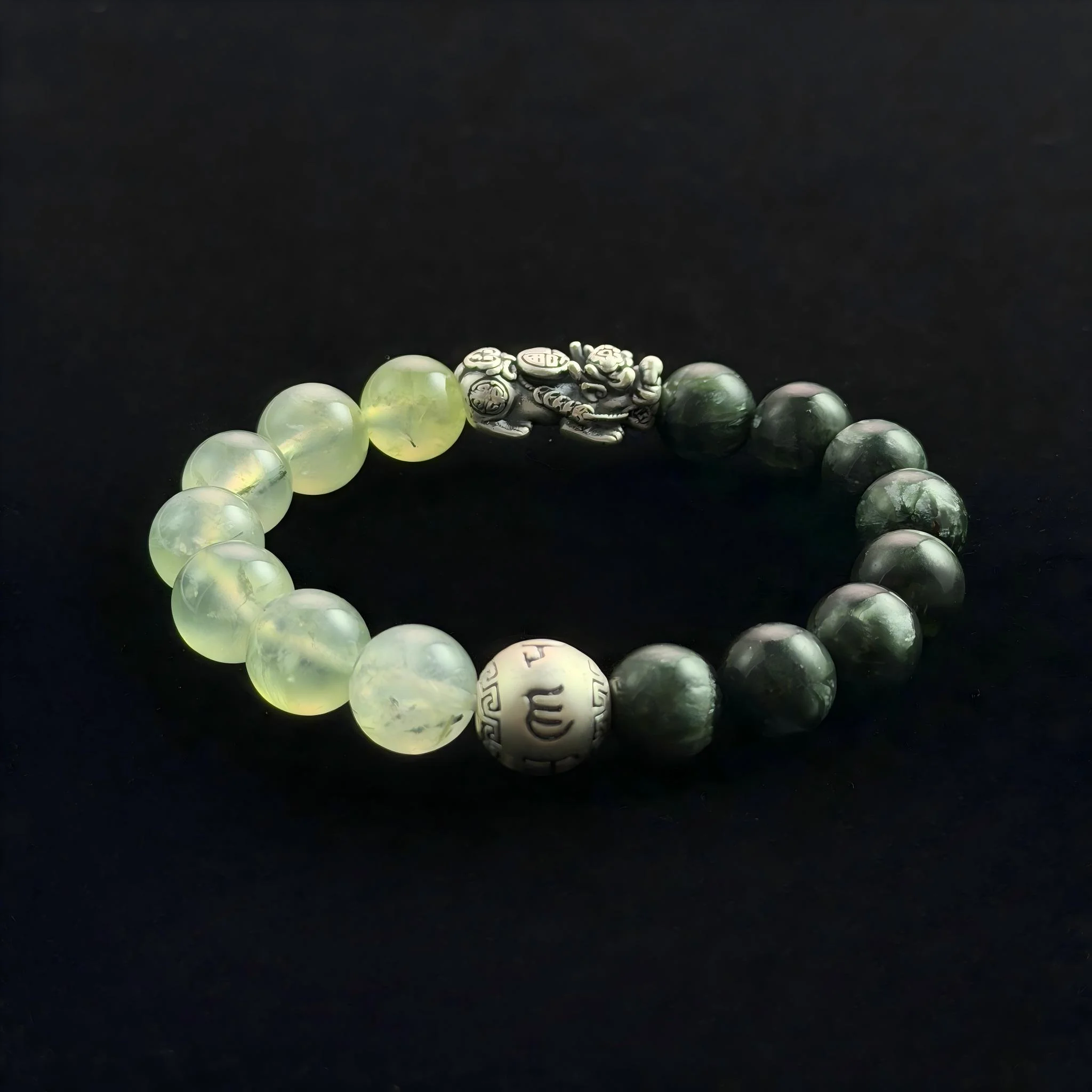 Feng Shui crystal bracelet with dark green Green Ghost beads, translucent Grape Stone (Prehnite) beads, a silver Pixiu wealth charm, and a silver mantra bead on a black background.