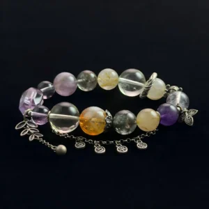 A top-down photograph of a natural crystal bracelet featuring round and rectangular Amethyst beads mixed with round Golden Rutilated Citrine "hair" quartz beads. The bracelet includes detailed silver metal charms, a leaf dangle, and a chain extension against a dark black textured background.