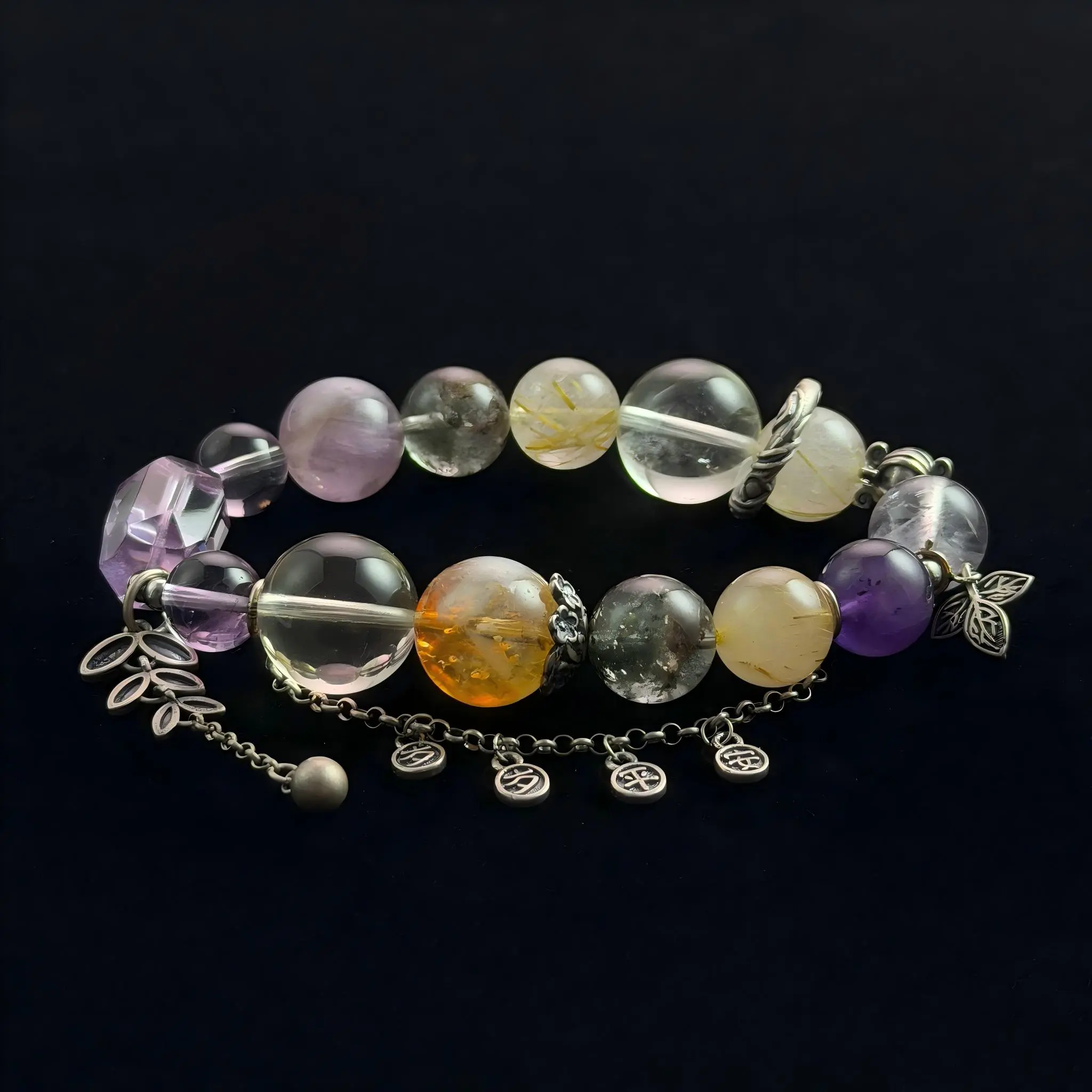 A top-down photograph of a natural crystal bracelet featuring round and rectangular Amethyst beads mixed with round Golden Rutilated Citrine "hair" quartz beads. The bracelet includes detailed silver metal charms, a leaf dangle, and a chain extension against a dark black textured background.