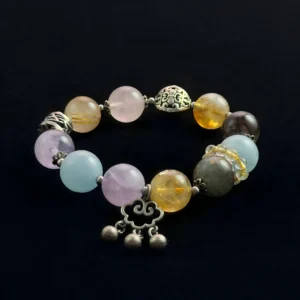 Natural crystal bead bracelet featuring light blue Aquamarine, yellow Golden Rutilated Quartz, purple Amethyst, and pink Rose Quartz stones with a silver Ruyi good luck charm on a black background